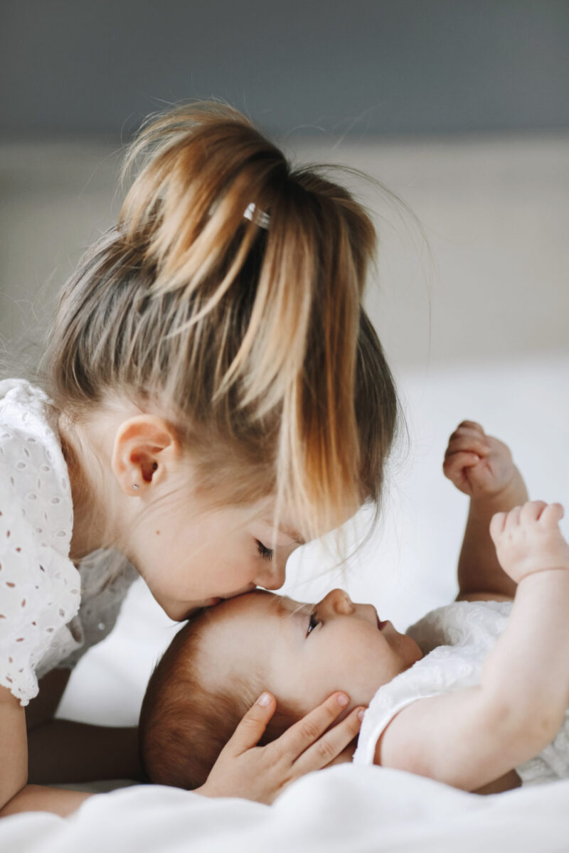 Front view of elder sister is kissing little baby girl in the fo